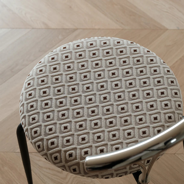 Round cushion with diamond pattern on a chair seat, on a wooden floor.