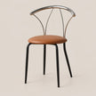 A modern dining chair with a curved backrest made of polished silver metal, a brown leather seat cushion, and slim black metal legs, shown against a solid light beige background.