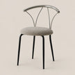 A modern dining chair with a round textured gray upholstered seat, black tapered legs, and a curved polished metal backrest, shown against a solid light beige background.