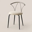 A modern dining chair with a textured cream bouclé seat cushion, black metal legs, and a curved polished silver metal backrest, set against a solid warm beige background.