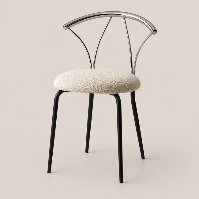 A modern dining chair with a textured cream bouclé seat cushion, black metal legs, and a curved polished silver metal backrest, set against a solid warm beige background.