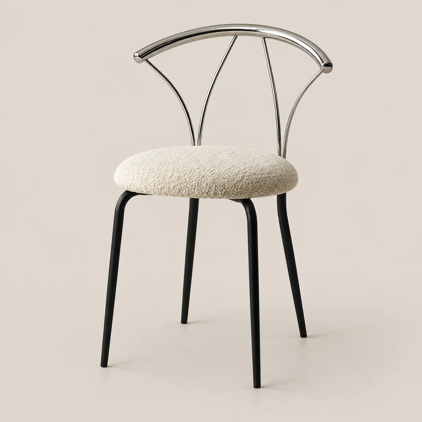 A modern dining chair with a textured cream bouclé seat cushion, black metal legs, and a curved polished silver metal backrest, set against a solid warm beige background.