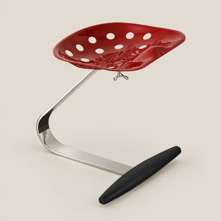 A modern red perforated seat with a curved chrome support base and a black footrest, photographed on a plain warm beige studio background.