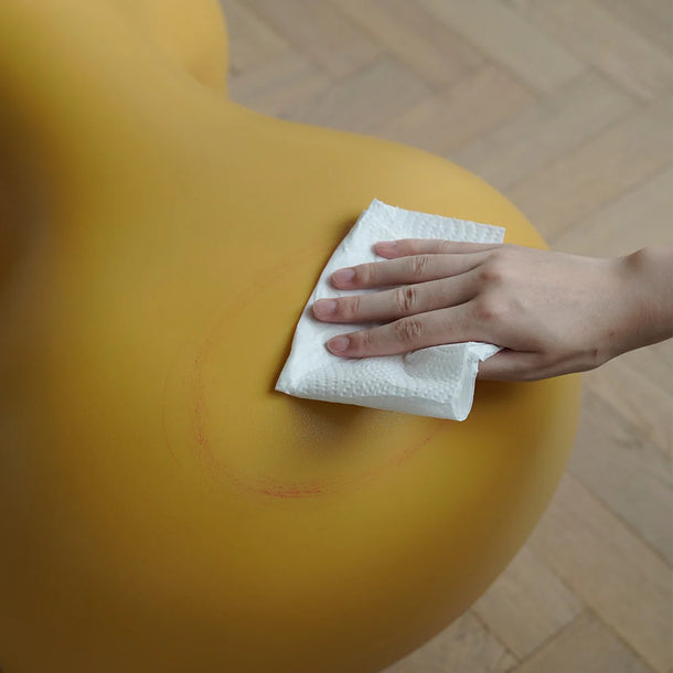Hand cleaning a yellow surface with a paper towel