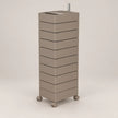 A tall, modern rolling storage cabinet with nine stacked drawers in a warm taupe-beige finish, featuring a metal top tray and four caster wheels, shown against a neutral light gray background.
