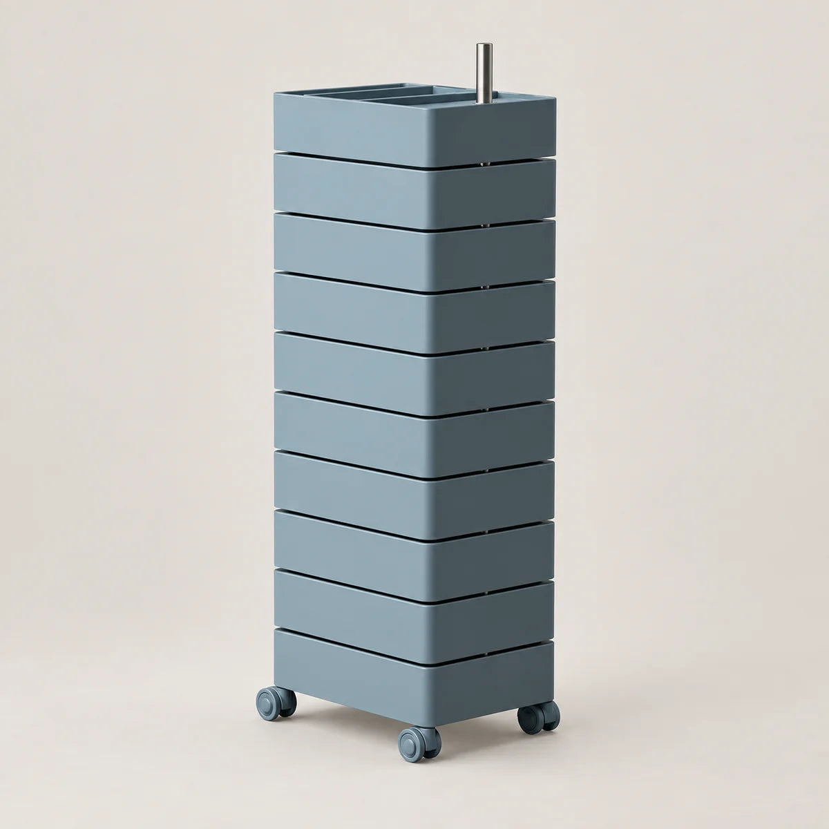 A tall, modern rolling storage unit with nine stacked rectangular drawers in a muted blue-gray color, featuring a square top with a sink-like recess and a small metal handle, set against a solid light beige background.