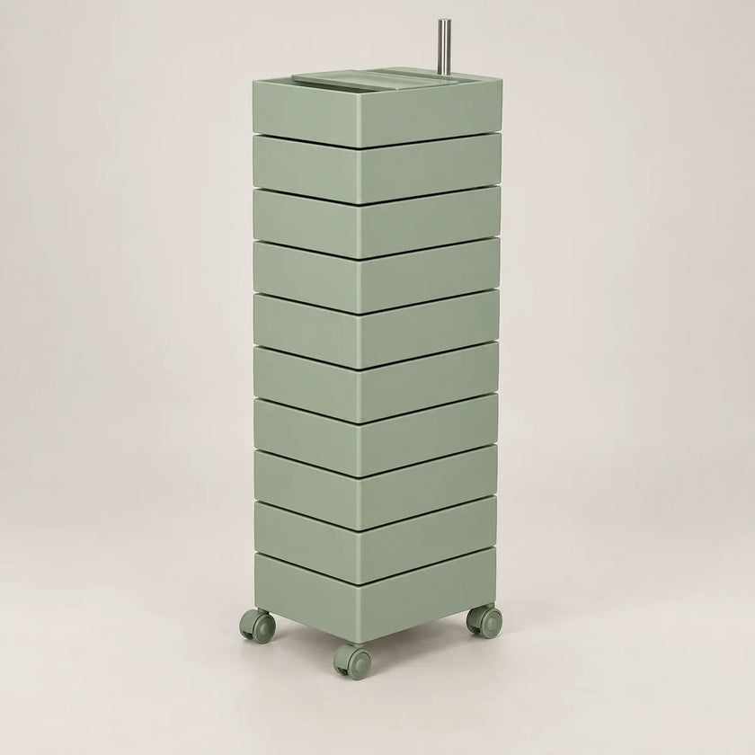 A tall, narrow rolling storage cart with multiple stacked drawers in a muted sage green color, featuring a metal handle on top and small caster wheels at the base, shown against a plain light gray studio background.