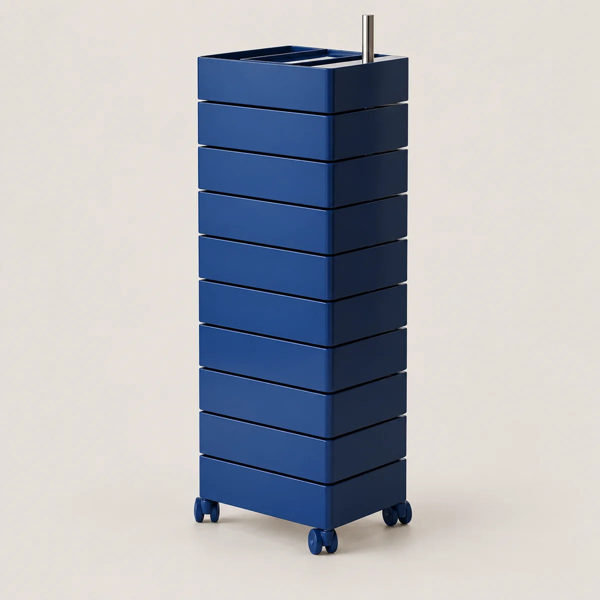 A tall, blue rolling organizer with multiple stacked drawers and a top tray holding a metal utensil, photographed on a clean light beige studio background.