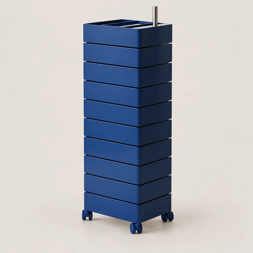 A tall, blue rolling organizer with multiple stacked drawers and a top tray holding a metal utensil, photographed on a clean light beige studio background.