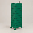 A tall, green rolling storage cabinet with multiple stacked drawers or compartments, a rectangular top, and small wheels on the base, photographed against a plain light beige studio background.
