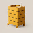 A mustard yellow rolling storage cart with five drawers and a top tray, shown on a plain warm beige background.