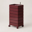 A dark burgundy rolling storage cart with six stacked drawers, a top tray, and a silver metal handle, shown on a light gray background.