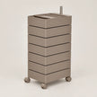 A modern, minimalist rolling storage cart with seven stacked drawers in a warm taupe-brown finish, featuring a matching top tray and dual metal handles, set against a solid light gray background.