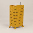 A mustard yellow rolling storage cabinet with six stacked drawers and a metal handle on top, shown on a plain light beige studio background.