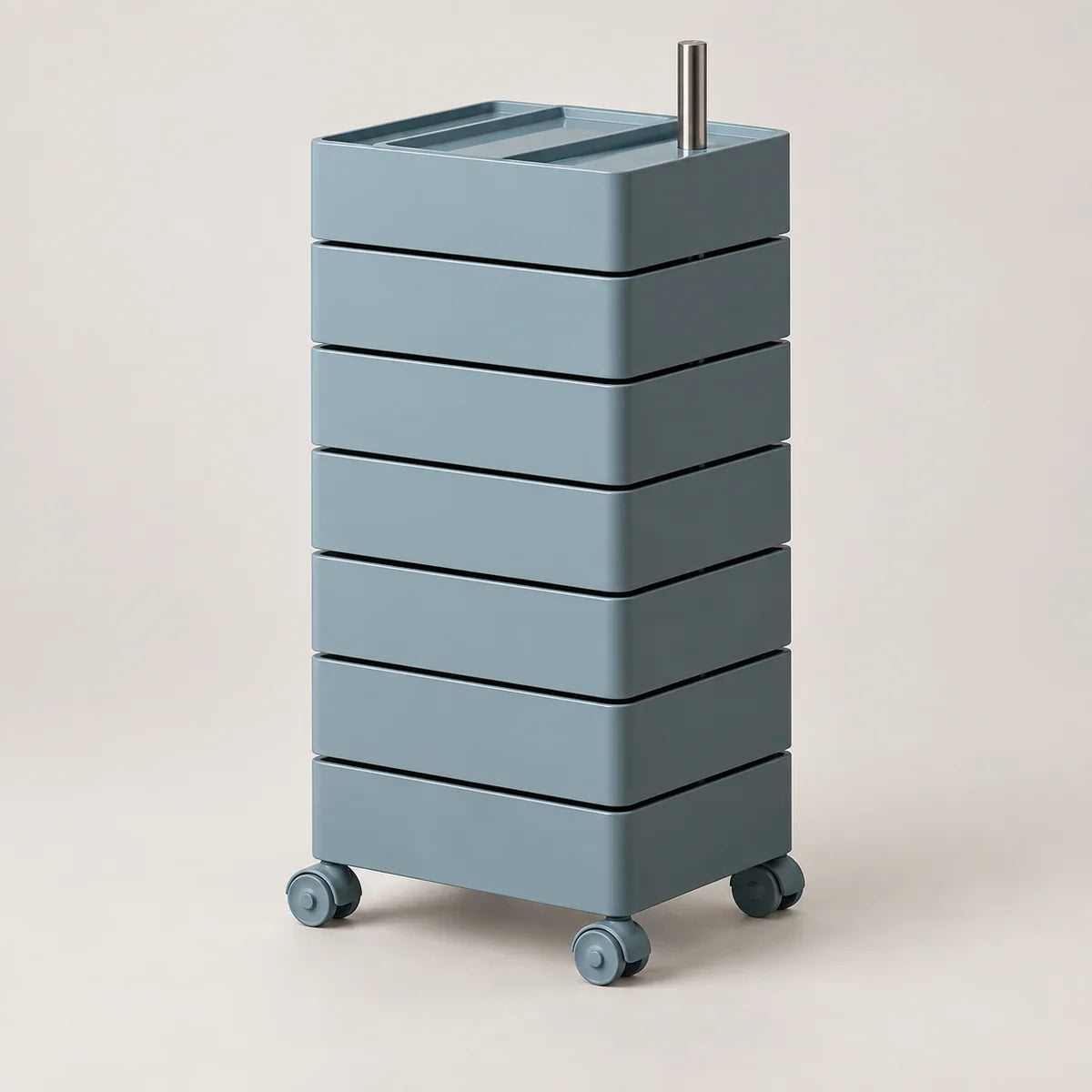 A tall, modular rolling storage cart with six stacked drawer-like compartments, finished in a muted dusty blue-gray color, featuring a silver metal handle on top and caster wheels at the base, set against a plain beige studio background.