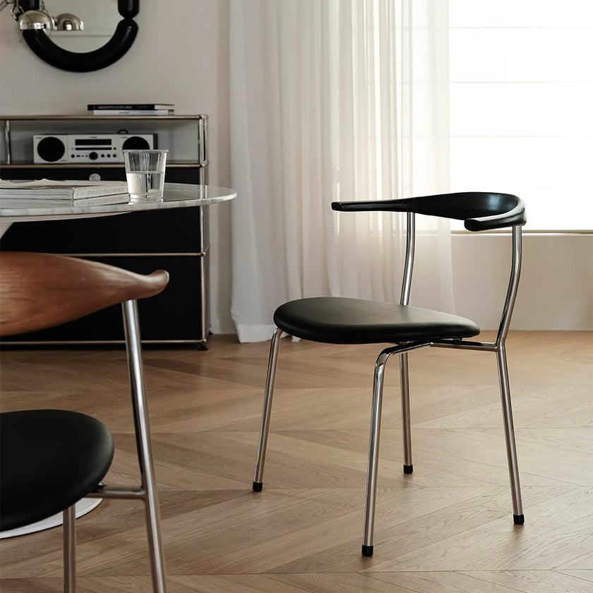 Modern black chair with metal legs in a room with a desk and curtains.