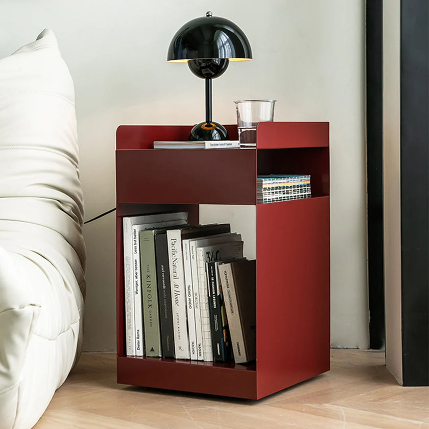 Red nightstand with books and a lamp next to a bed