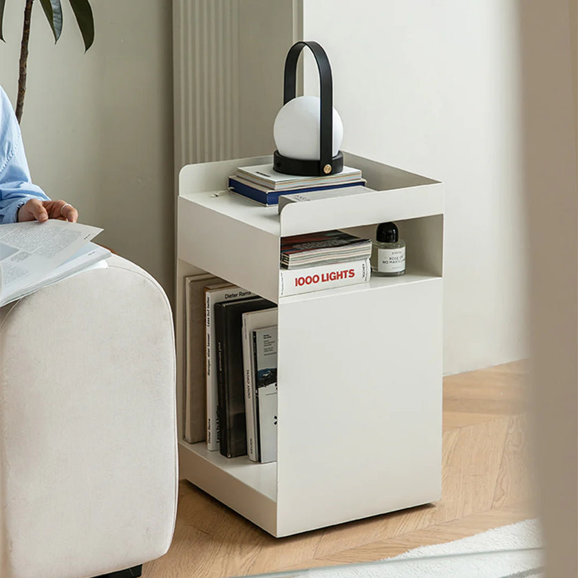 White side table with books and a lamp next to a person sitting on a chair.
