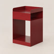 A modern, minimalist red metal side table with a geometric open design, photographed on a neutral light beige background.