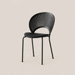 A modern black metal dining chair with a slatted oval backrest and four slim legs, shown against a solid light beige background.