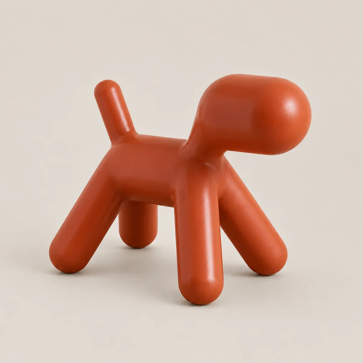 A modern, stylized dog-shaped stool in a matte terracotta orange color, photographed on a clean, solid, light beige background.