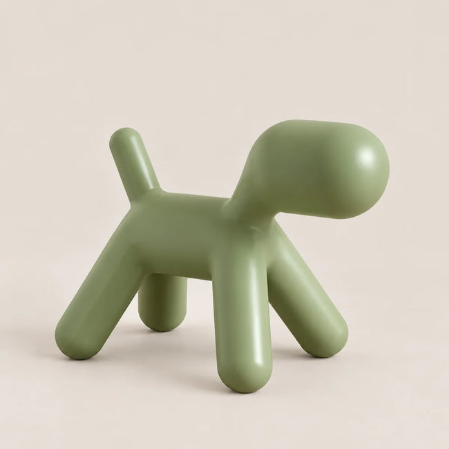 A minimalist, dog-shaped stool in a matte sage green color, photographed on a clean, solid, warm off-white background.