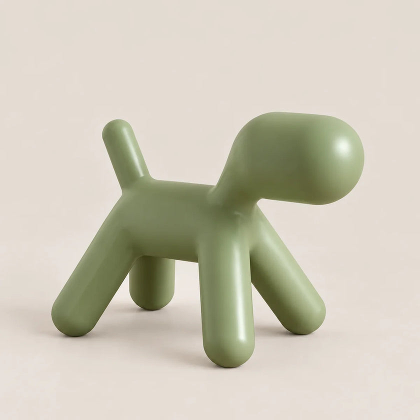 A minimalist, dog-shaped stool in a matte sage green color, photographed on a clean, solid, warm off-white background.