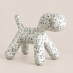 A modern, dog-shaped stool or ottoman with a white textured surface covered in small black speckles, set against a solid, warm off-white background.