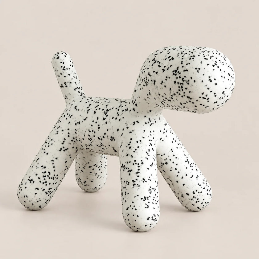 A modern, dog-shaped stool or ottoman with a white textured surface covered in small black speckles, set against a solid, warm off-white background.