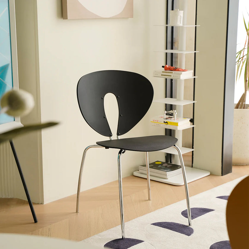Modern black chair with metal legs in a room with a bookshelf and window.