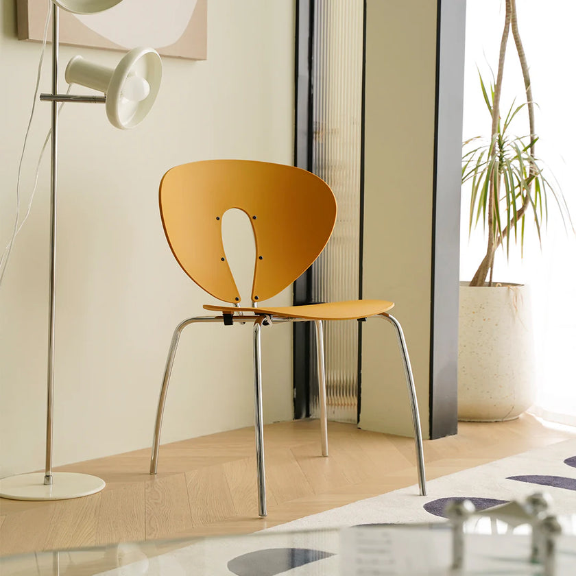 Modern chair with a yellow seat and backrest in a room with a lamp and plant.