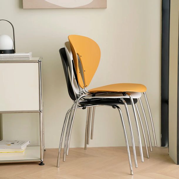 Three orange chairs stacked against a beige wall with a side table and lamp in the background.