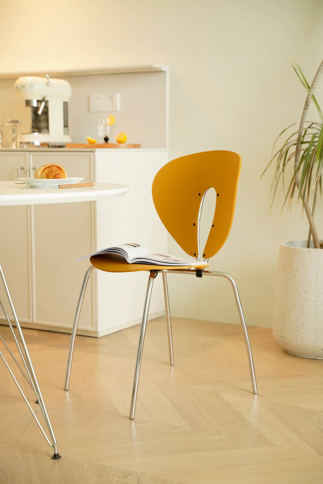 Yellow chair with a magazine on a wooden floor in a room with a plant and kitchen counter.