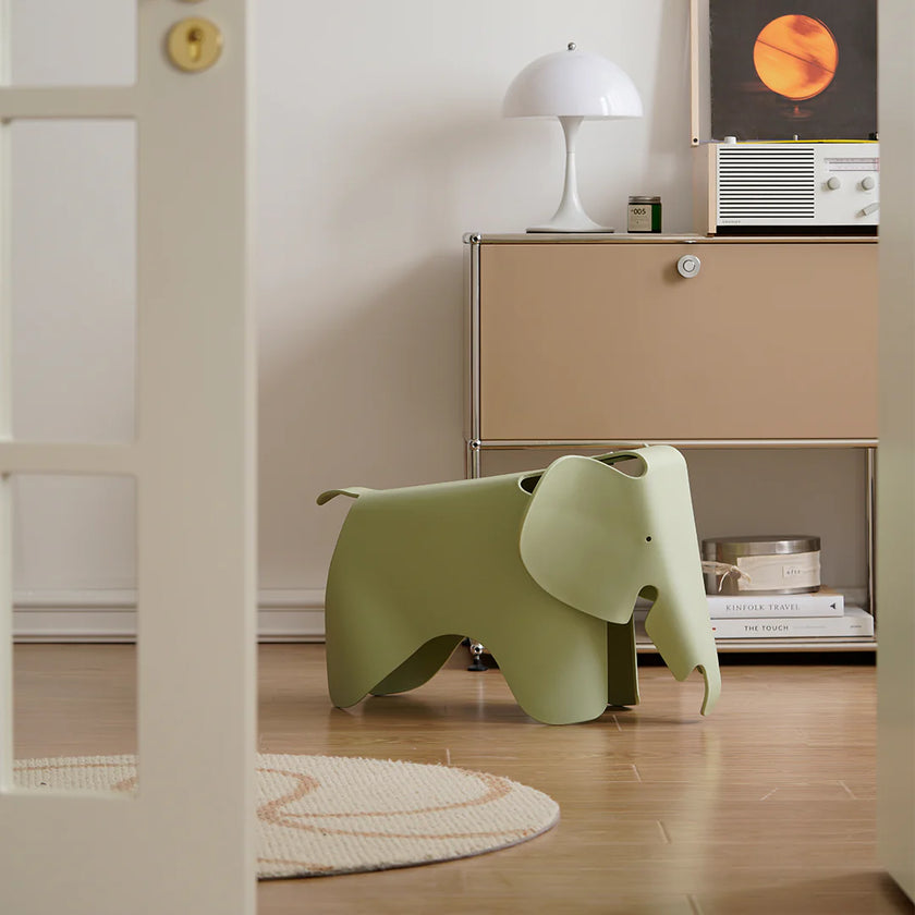 Green elephant-shaped stool in a room with a lamp and cabinet.