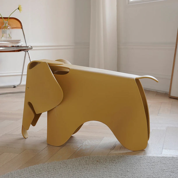 Yellow elephant-shaped stool in a room with a chair and window.