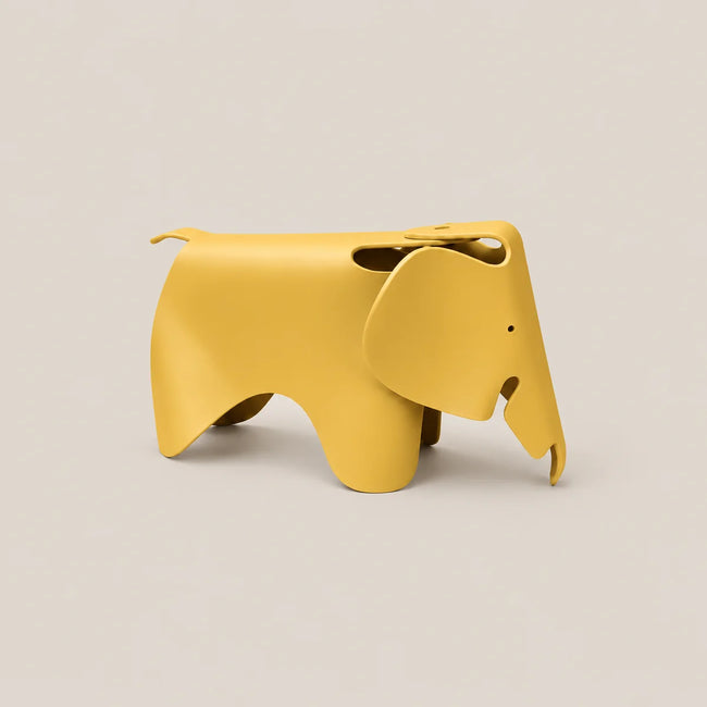 A minimalist yellow elephant-shaped metal stool on a solid light beige background.