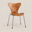 A mid-century modern style chair with a curved, sculptural wooden seat and backrest, supported by slim chrome metal legs with black rubber feet, set against a solid light beige background.