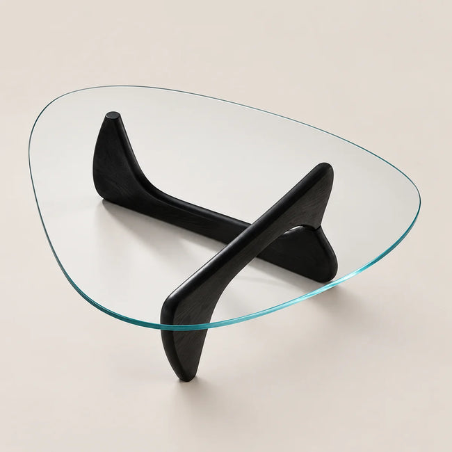 Triangular glass coffee table with a sculptural black wooden base, photographed on a warm beige background.
