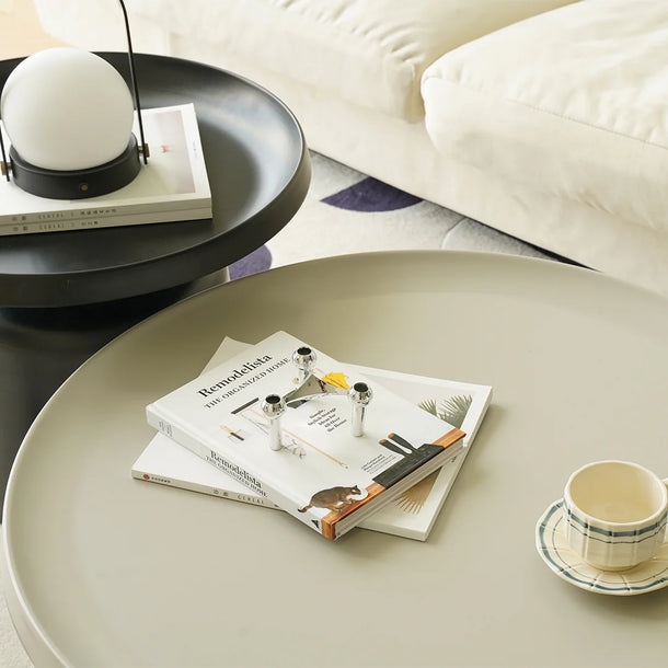 Round beige coffee table with books and a cup on a living room setting