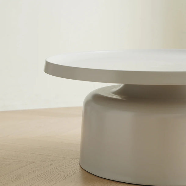 Round coffee table with a white top and beige base on a wooden floor.