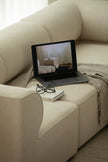 Laptop on a beige sofa with a book and glasses next to it