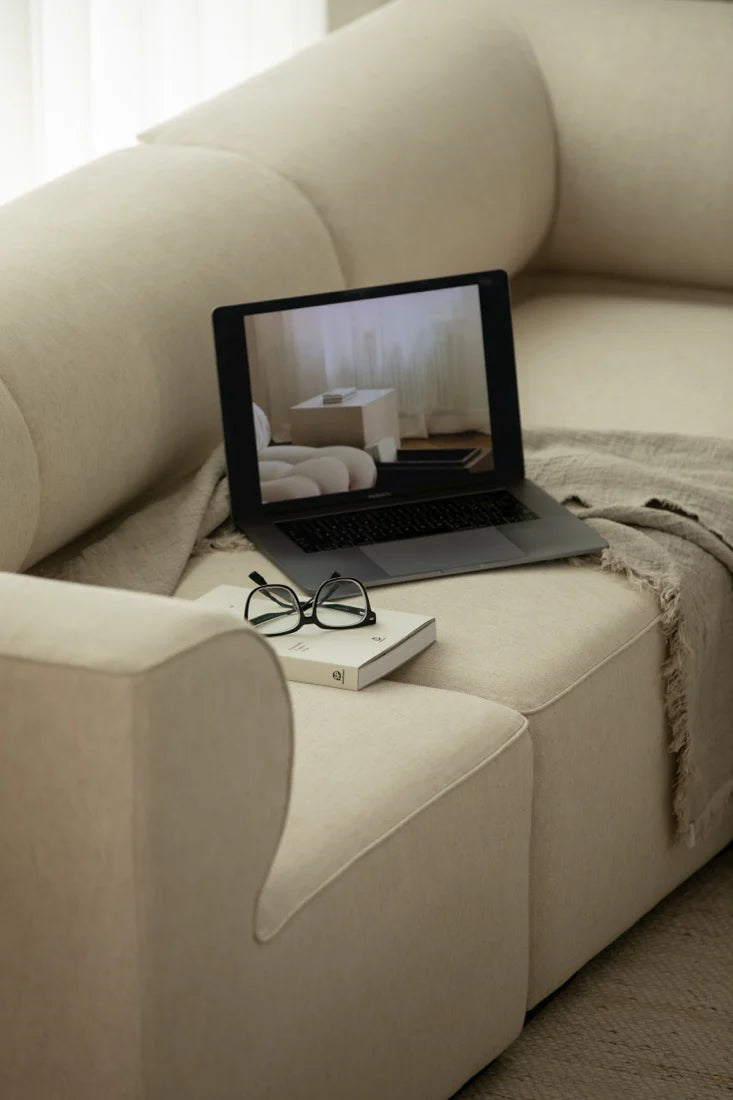 Laptop on a beige sofa with a book and glasses next to it