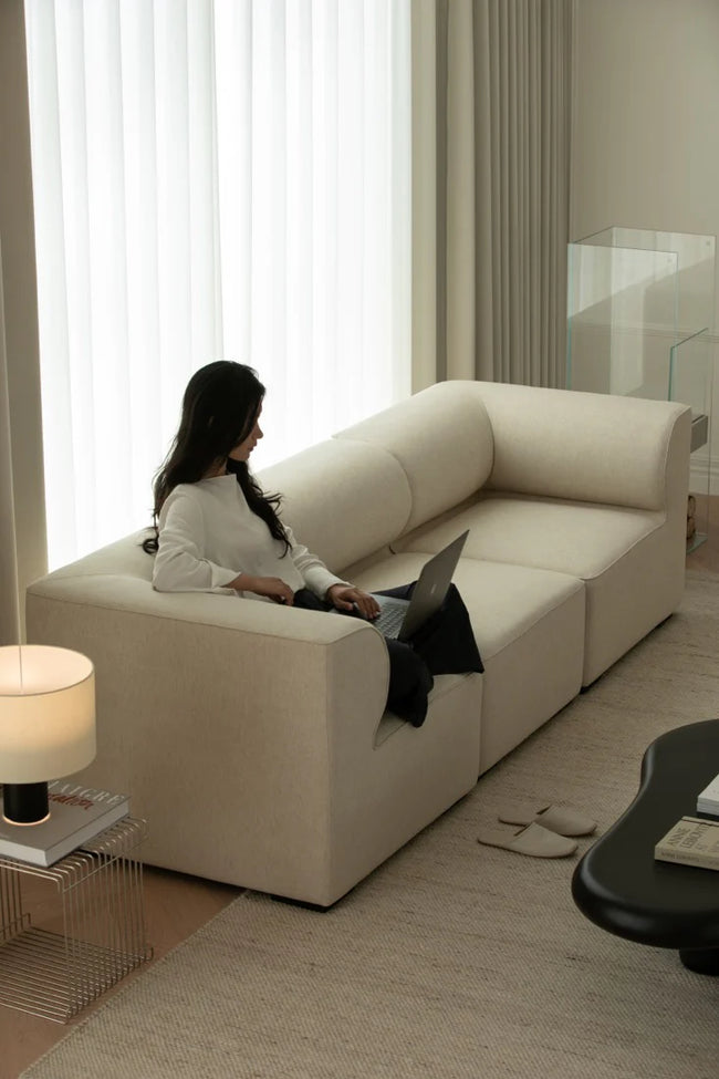 Woman using a laptop on a beige sectional sofa in a modern living room.