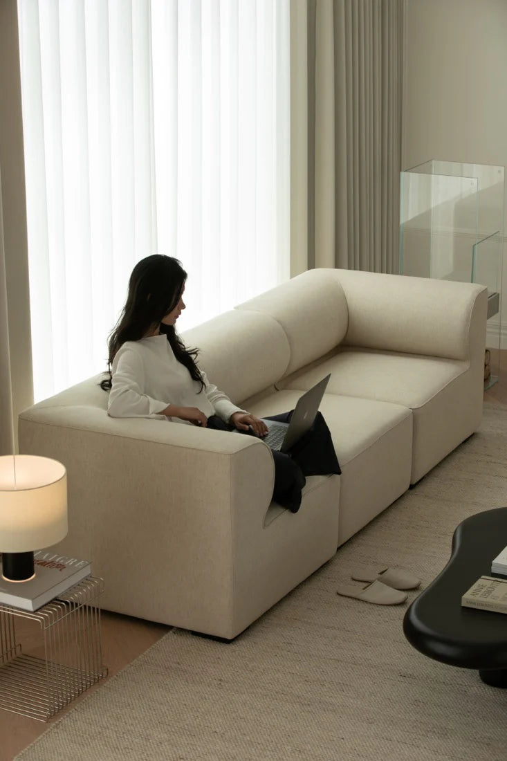 Woman using a laptop on a beige sectional sofa in a modern living room.