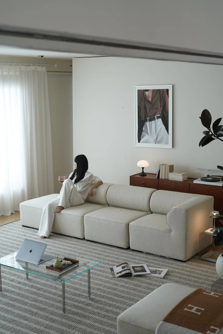 Woman sitting on a white sofa in a modern living room with a glass coffee table and decor items.