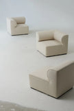 Three beige armchairs on a white floor with a plain white wall background