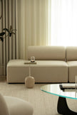 Beige sectional sofa in a living room with a glass coffee table and decorative items.