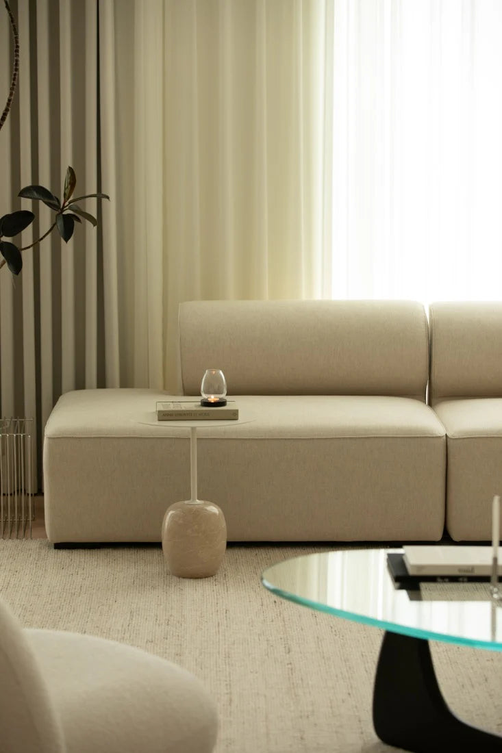 Beige sectional sofa in a living room with a glass coffee table and decorative items.