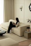 Woman reading a book on a beige sofa in a modern living room.