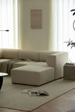 Beige sectional sofa in a living room with a rug and a small table.